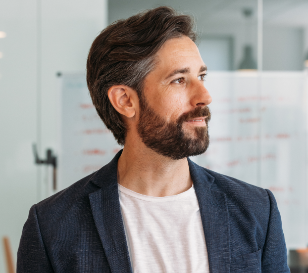 A bearded man in a white shirt stands confidently in front of a whiteboard, ready to present his ideas.