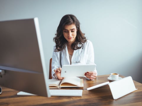 Portrait of adult female doctor sitting at desk in office clinic.