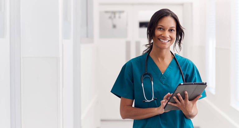 Portrait Of Smiling Female Doctor Wearing Scrubs In Hospital Corridor Holding Digital Tablet