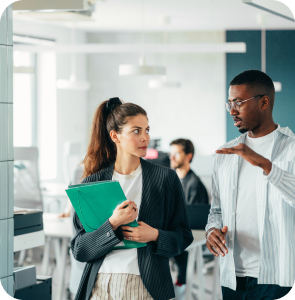 Two individuals engaged in a conversation within a professional office environment, surrounded by desks and office equipment.